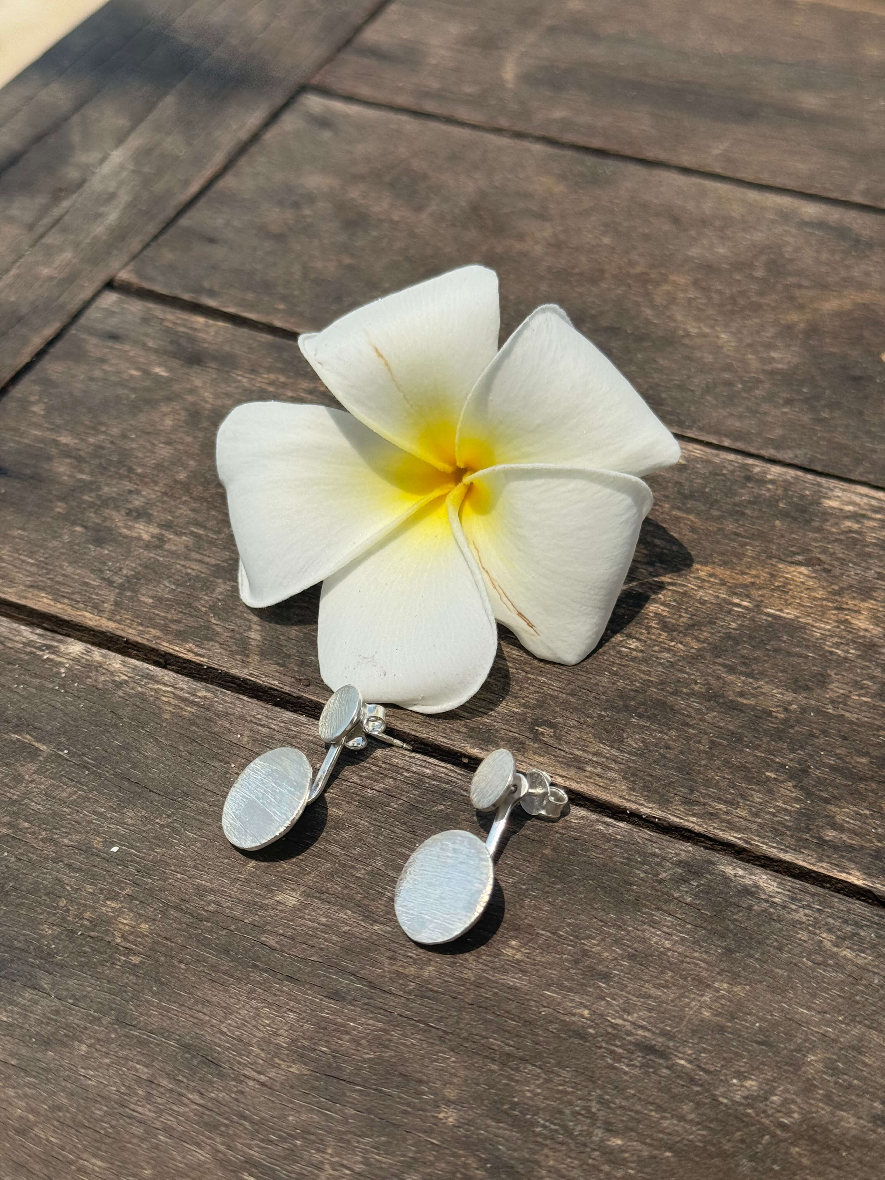 White flower with yellow center and silver earrings on a wooden surface