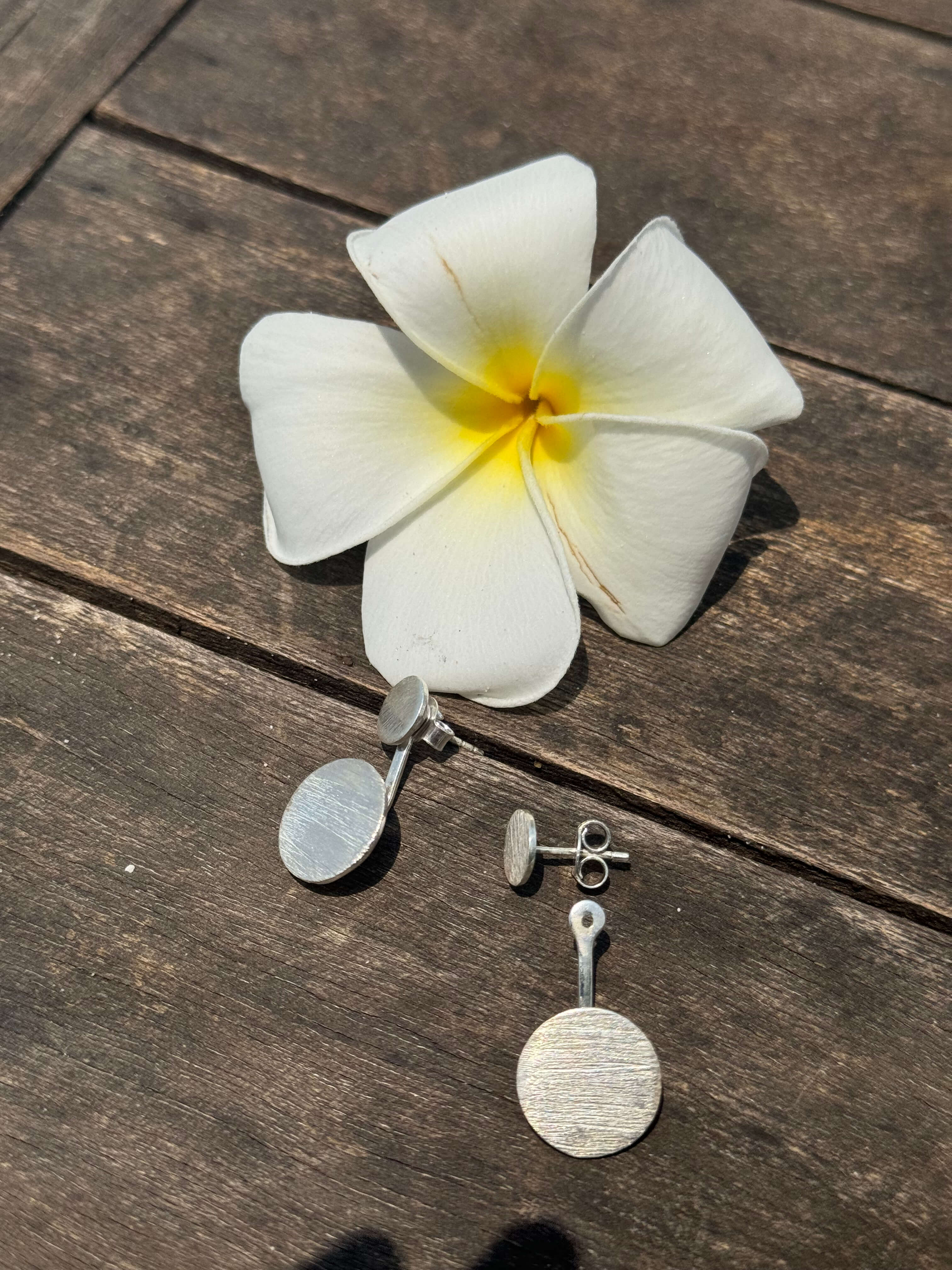 Pair of silver earrings with round pendants on a white flower on a wooden surface