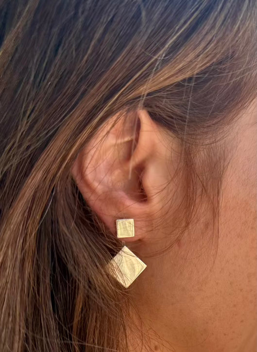 Gold square earrings worn by a person with brown hair.