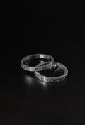 Two silver rings with intricate patterns on a black background
