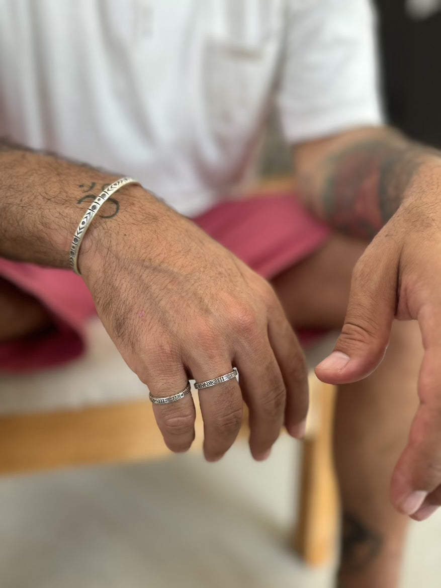 Close-up of a person's hands with tattoos, wearing a ring and bracelet.