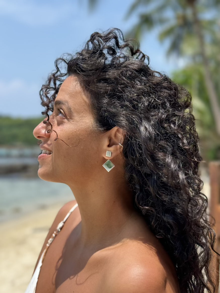 Woman with curly hair on a beach, wearing green earrings.
