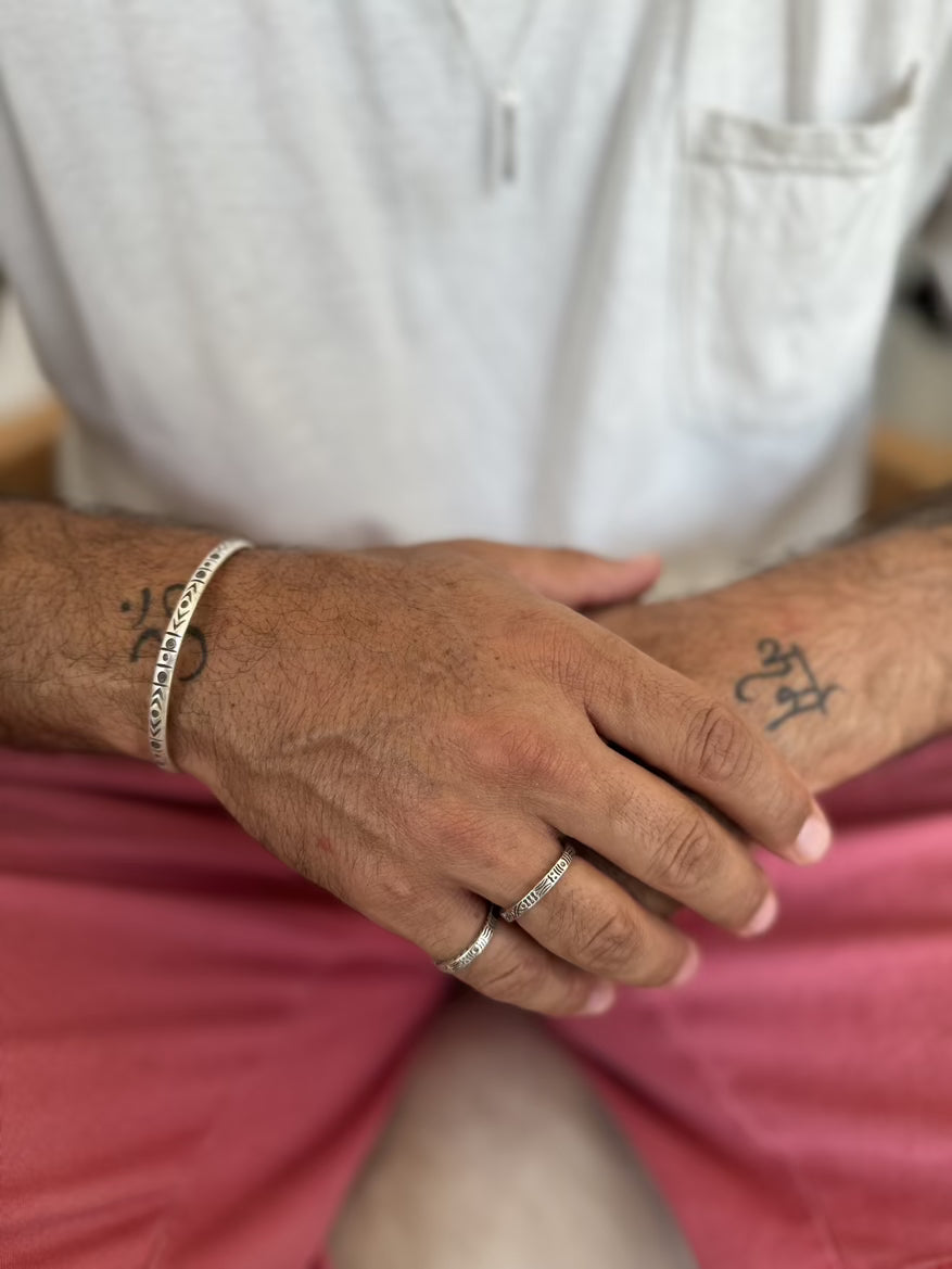Close-up of a person's hand with tattoos and rings, wearing a bracelet, on a blurred background.