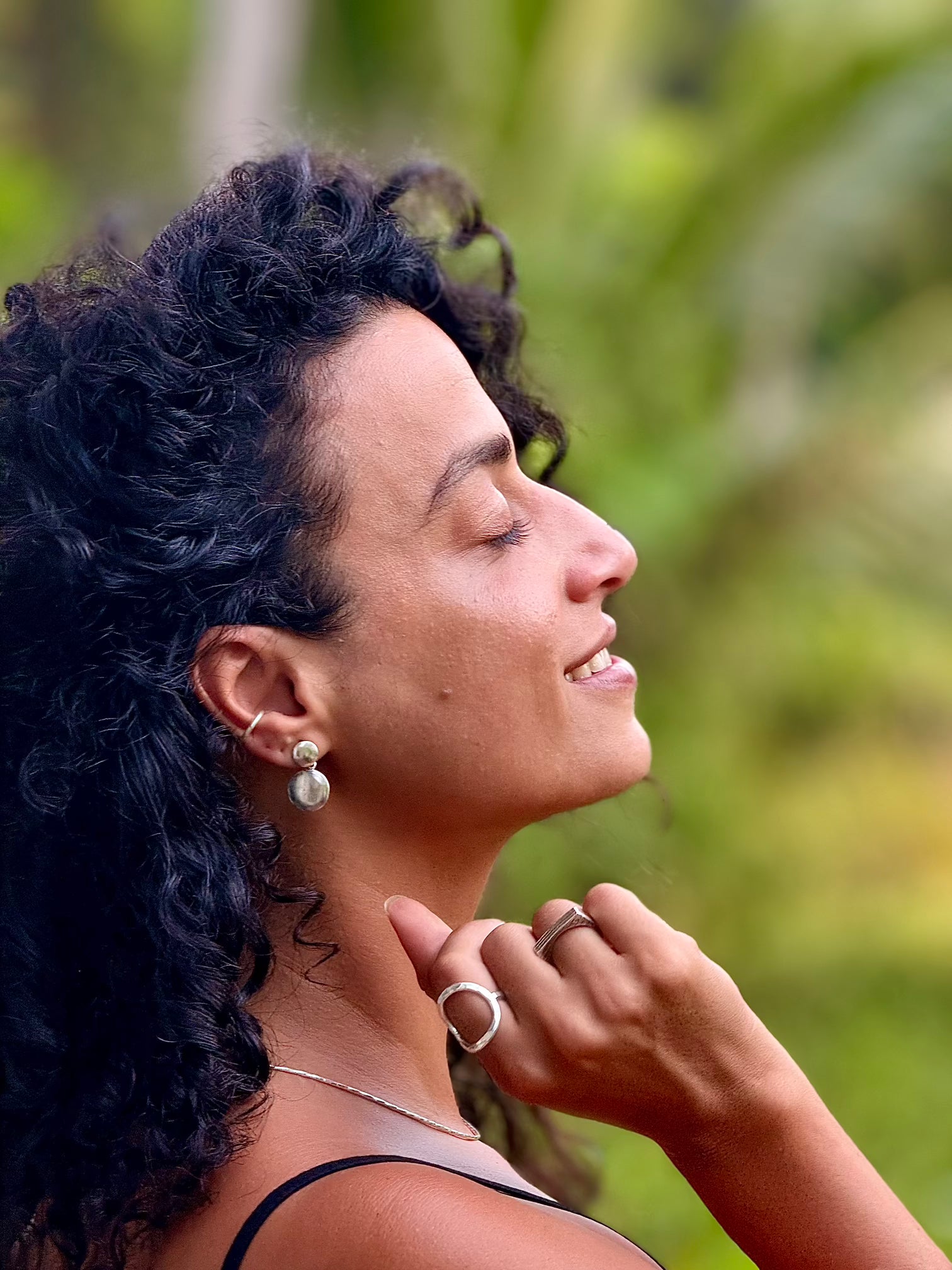 Woman with dark hair and earrings against a blurred green background
