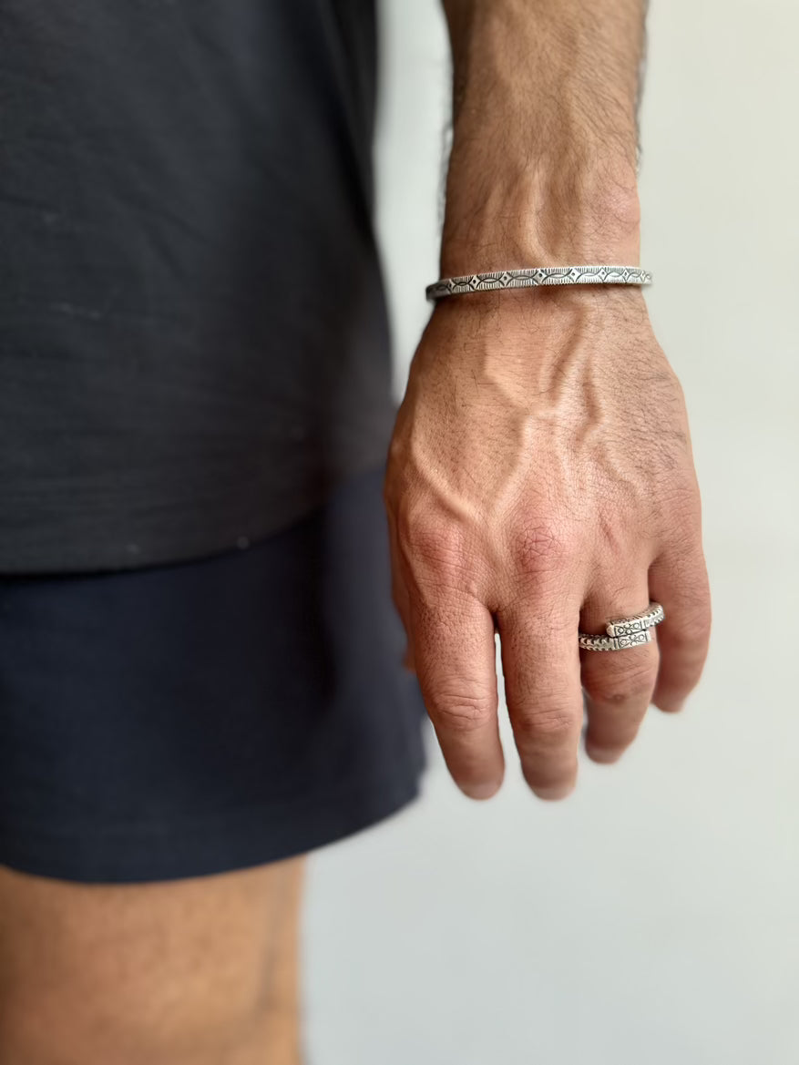 Hand wearing a silver bracelet and ring on a neutral background