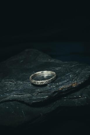 Silver ring with engraved design on a dark stone surface