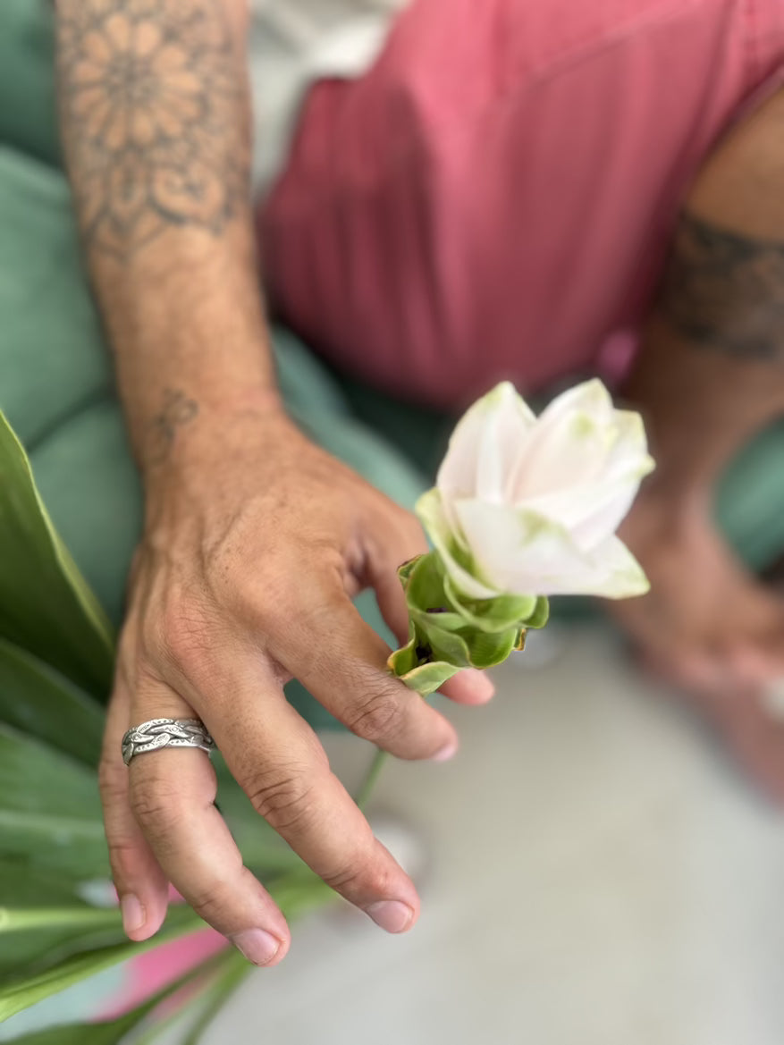 Person holding a white flower with green leaves, wearing a ring.