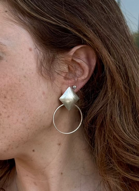 Close-up of a person wearing silver hoop earrings with a geometric stud.