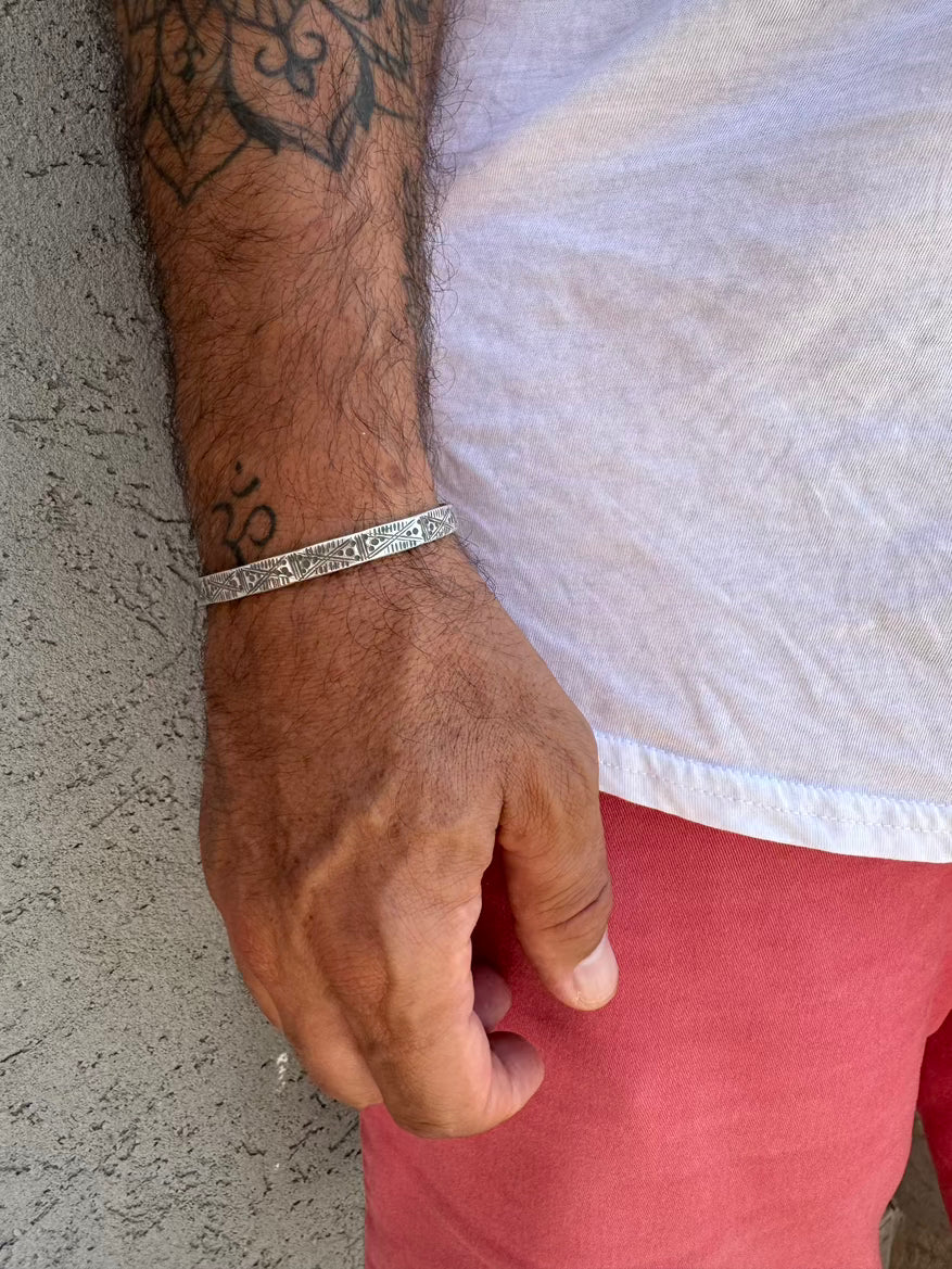 Close-up of a person's arm with a tattoo wearing a silver bracelet on a textured surface.