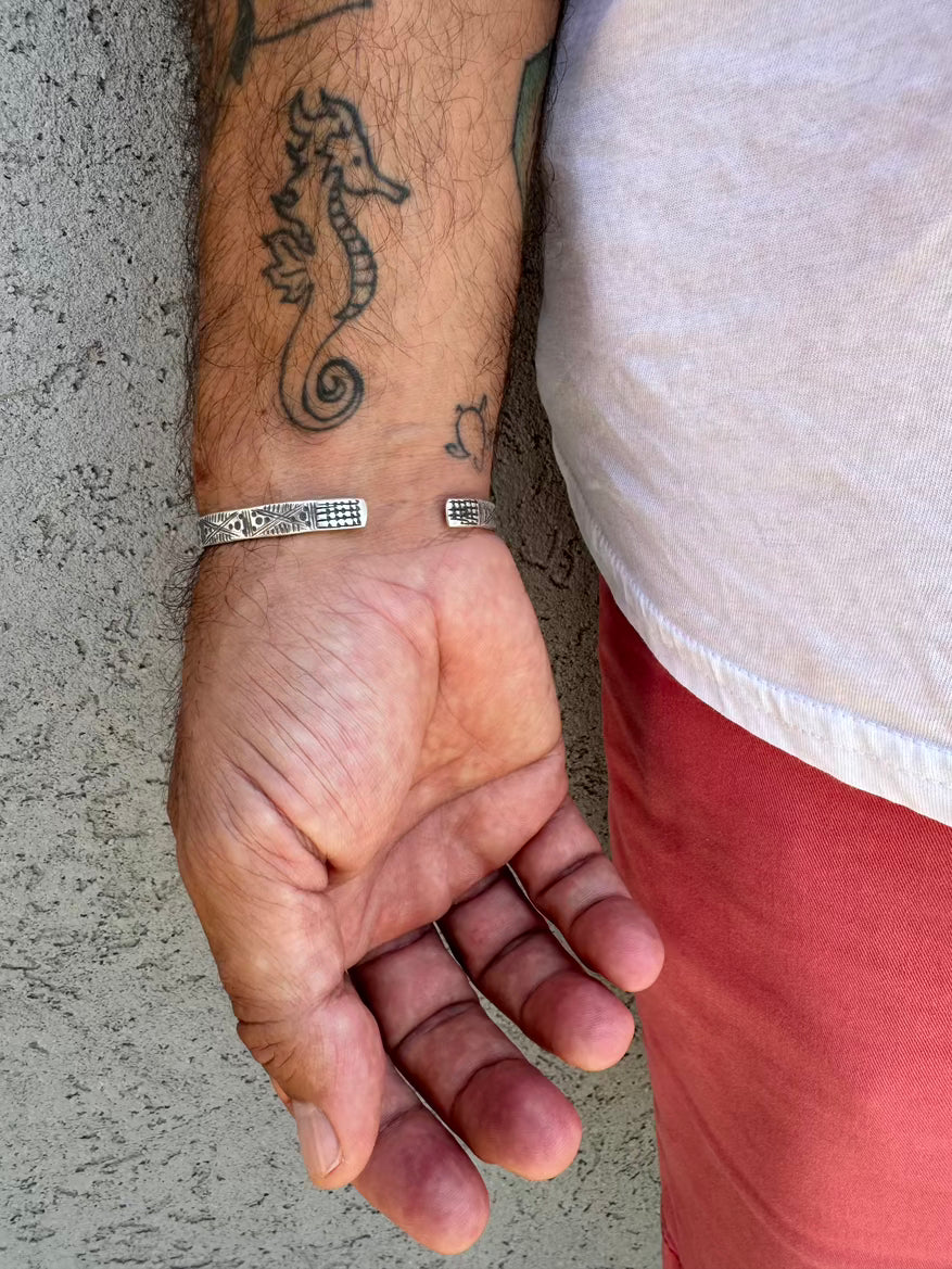 Hand with seahorse tattoo and silver bracelet on a concrete surface