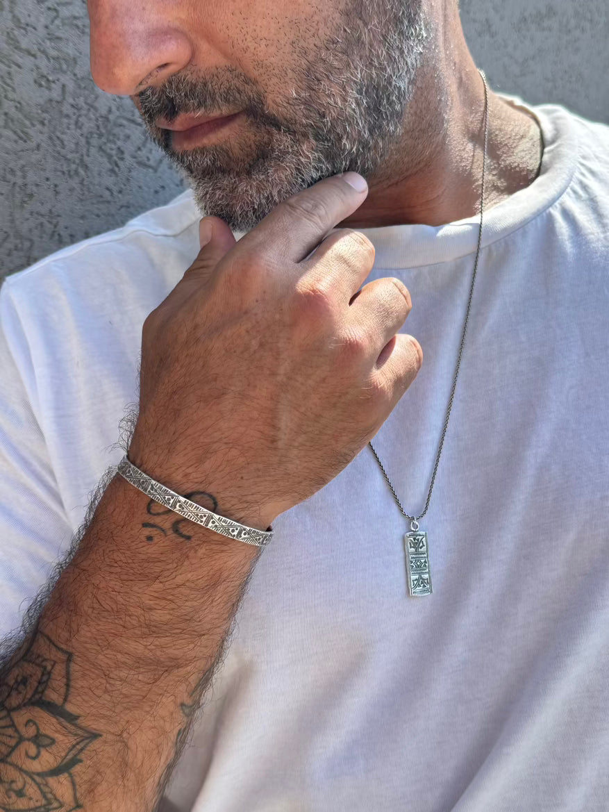 Man wearing a silver bracelet and necklace, with a neutral background