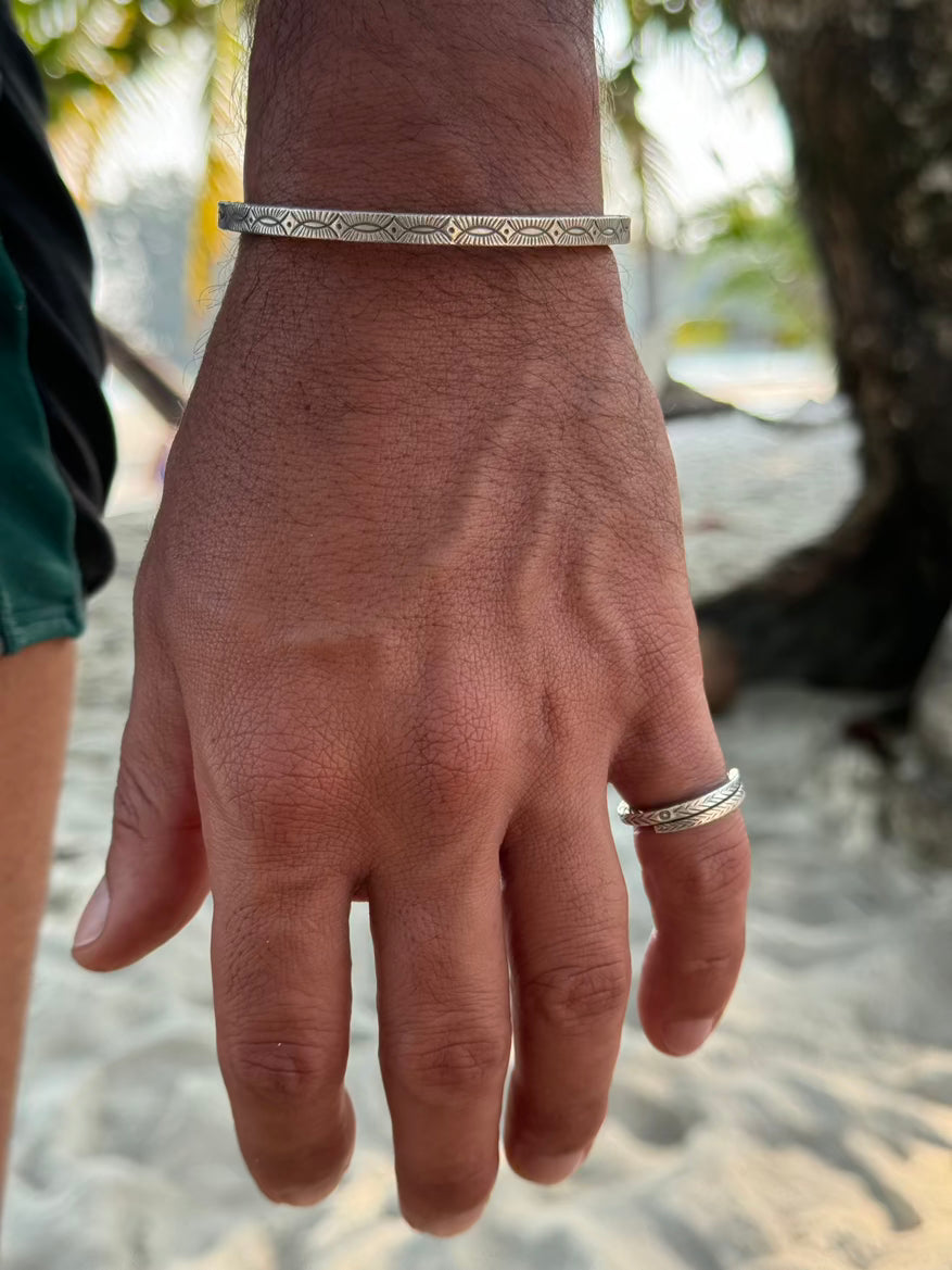 Hand wearing a silver bracelet and ring with a blurred natural background
