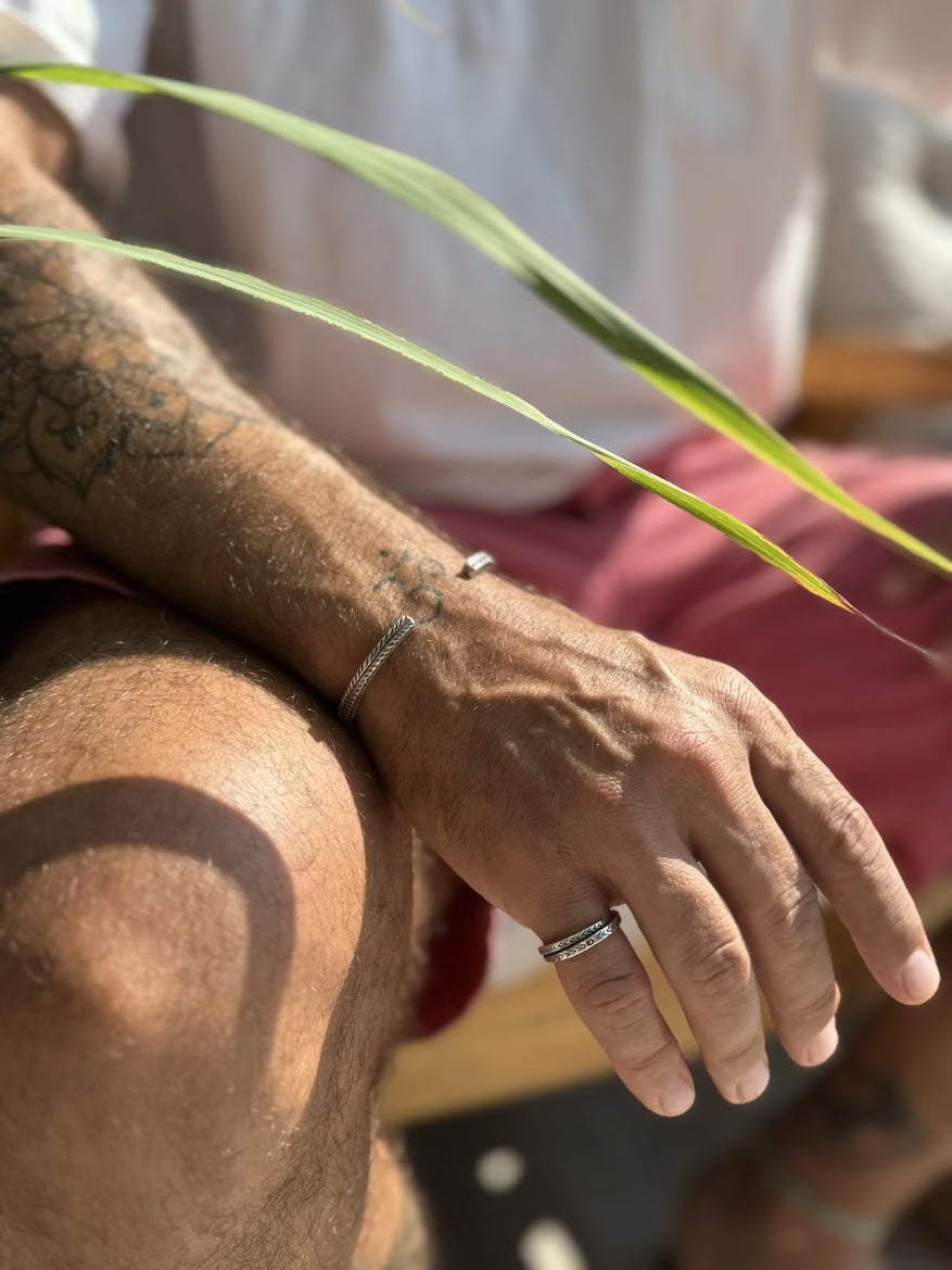 Close-up of a person's hand with rings and a bracelet, holding a plant leaf.