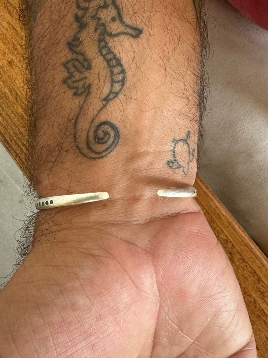 Close-up of a wrist with a seahorse tattoo and two silver rings.