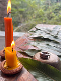 Two lit candles on a wooden surface with leaves and a ring in the background.