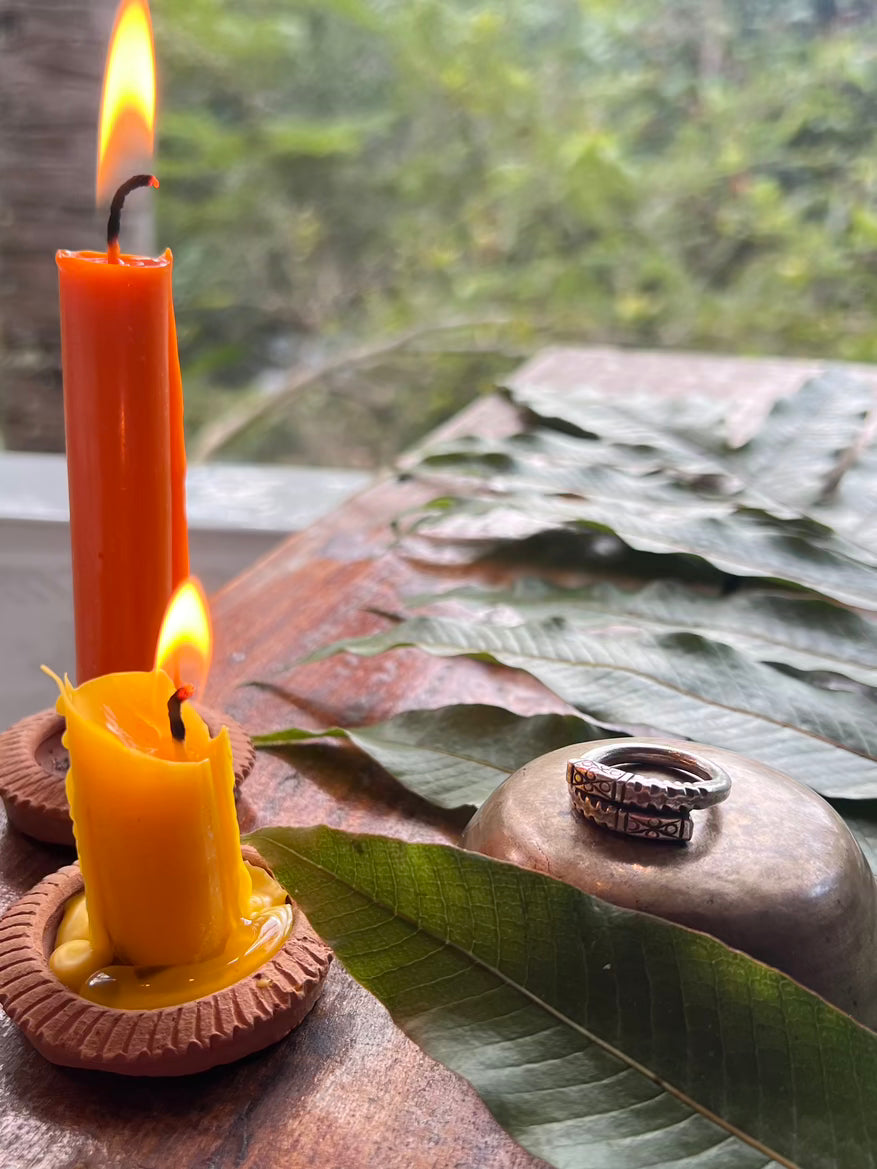 Two lit candles on a wooden surface with leaves and a ring in the background.