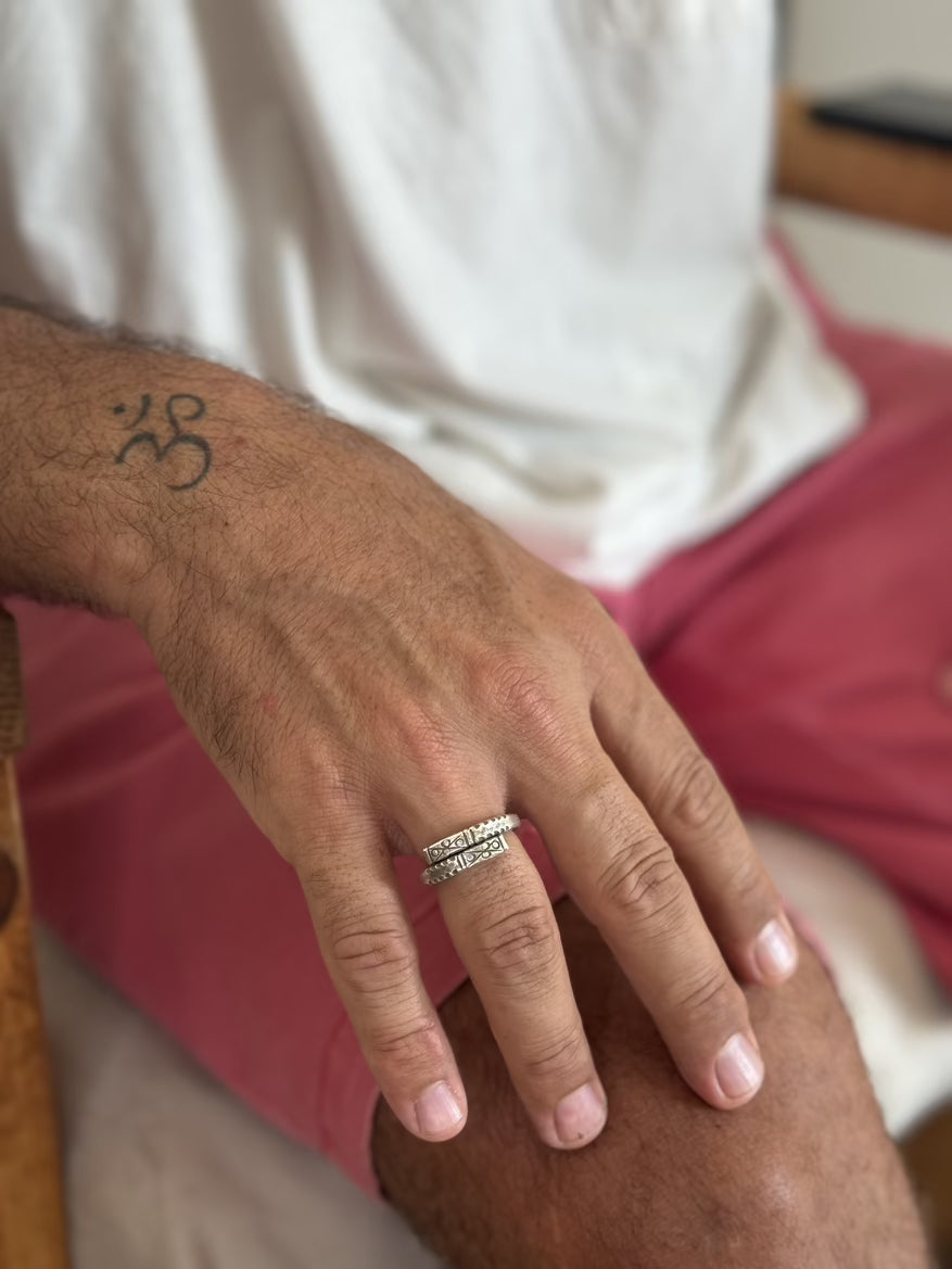 Hand with ring and tattoo on arm, wearing a white shirt and pink shorts.