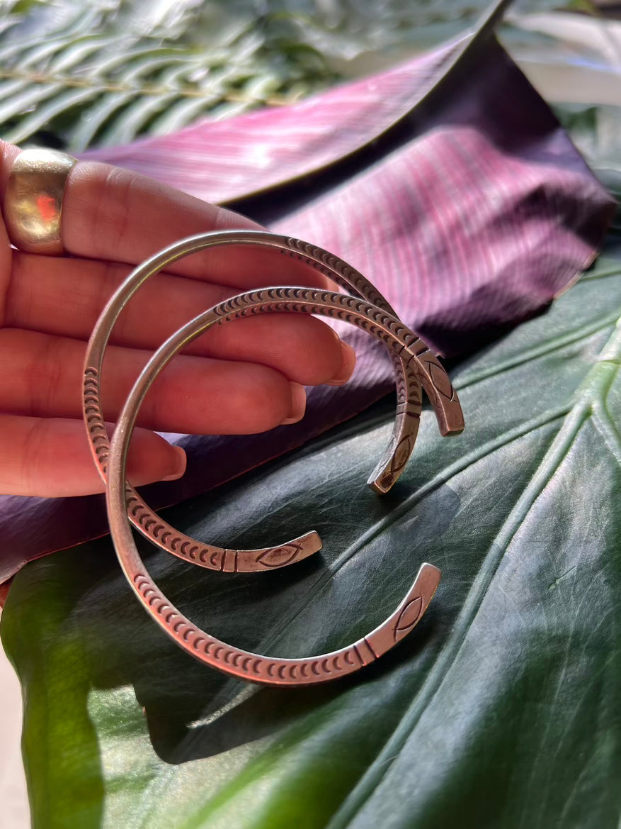 Two bronze bracelets on a hand with a leaf background