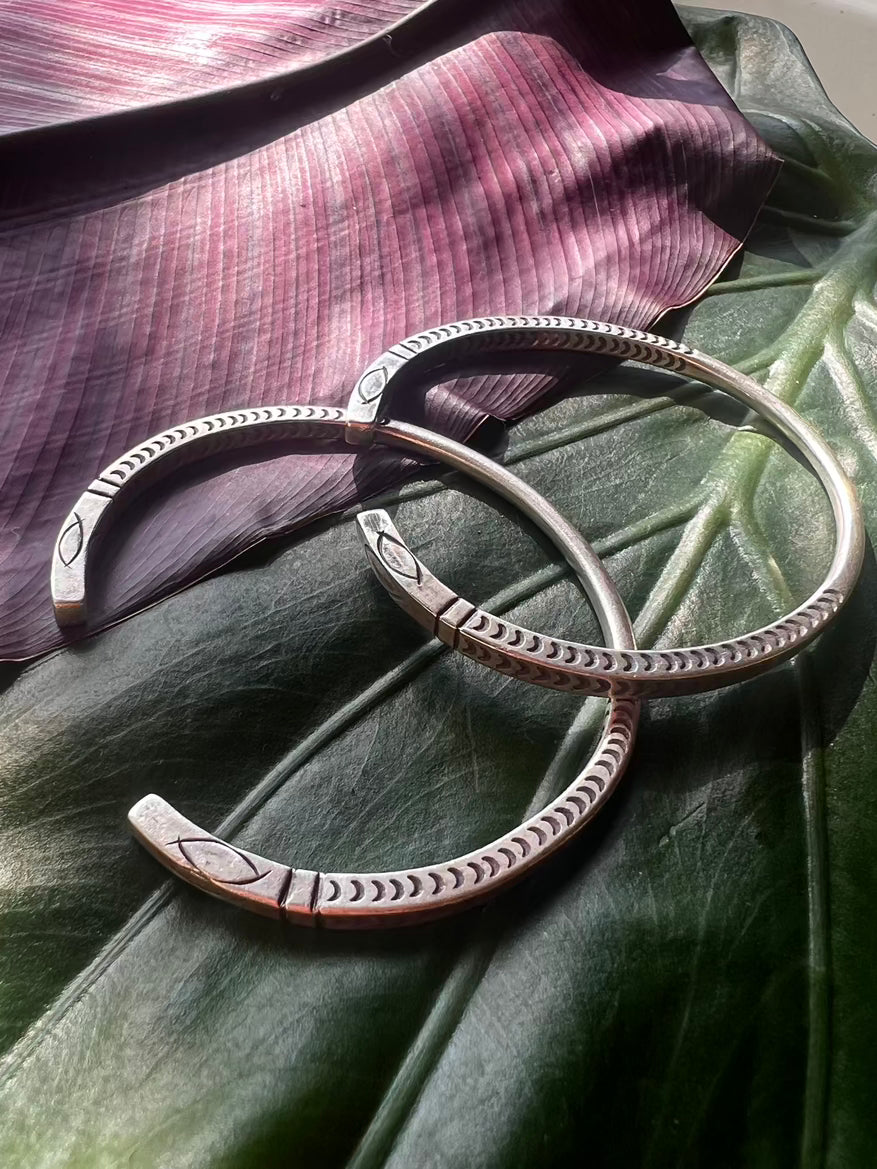 Two silver bracelets with intricate designs on a large green leaf.