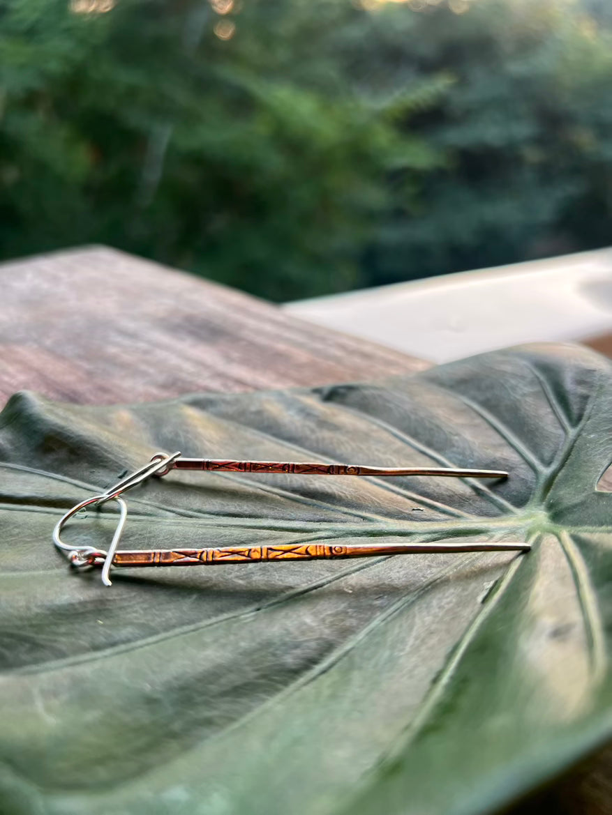 Two copper-colored hairpins on a large green leaf with a blurred natural background