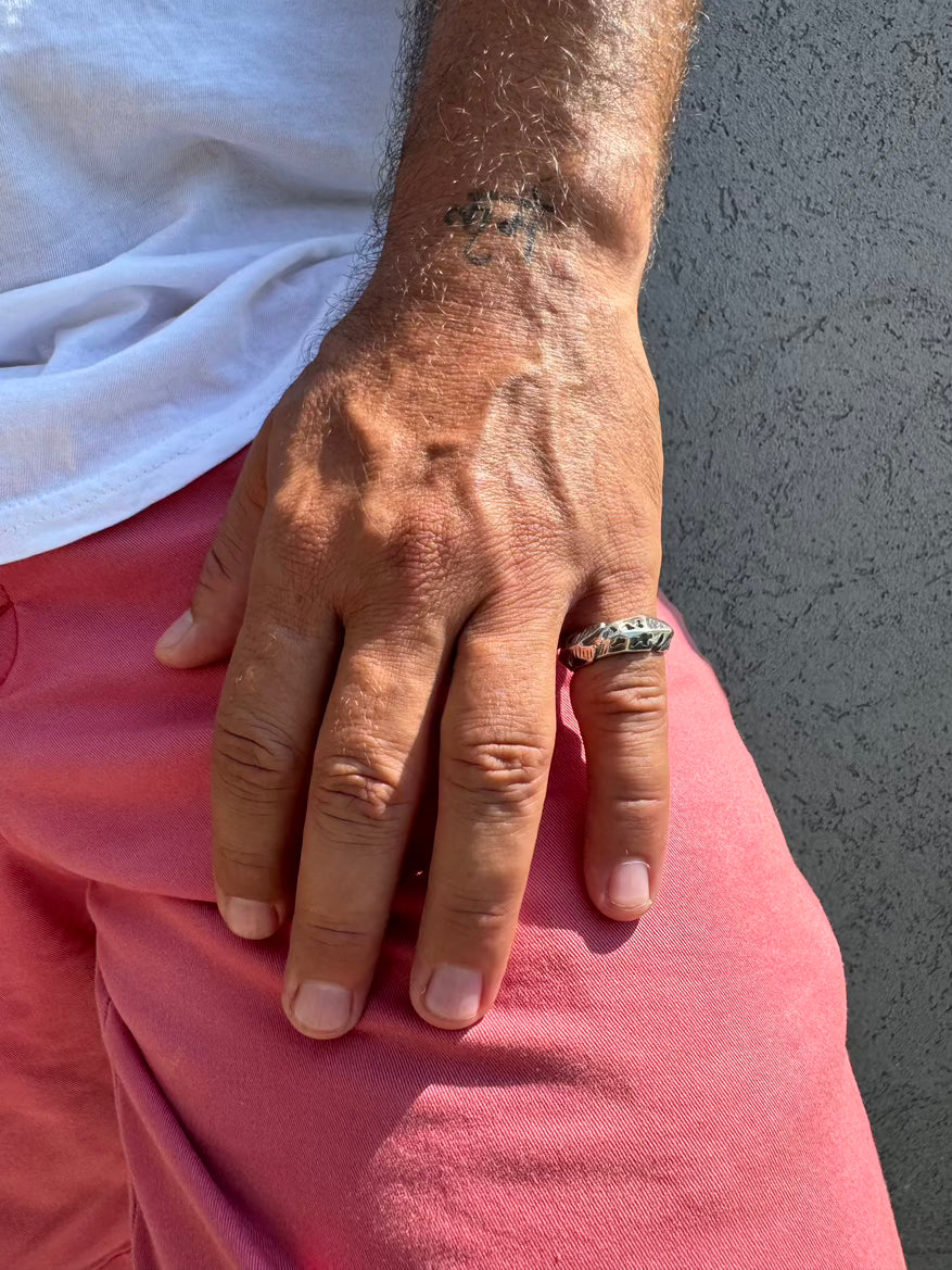 Hand with a ring on a person wearing a white shirt and red shorts against a gray wall.