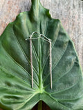 Silver earrings on a large green leaf with a wooden surface background