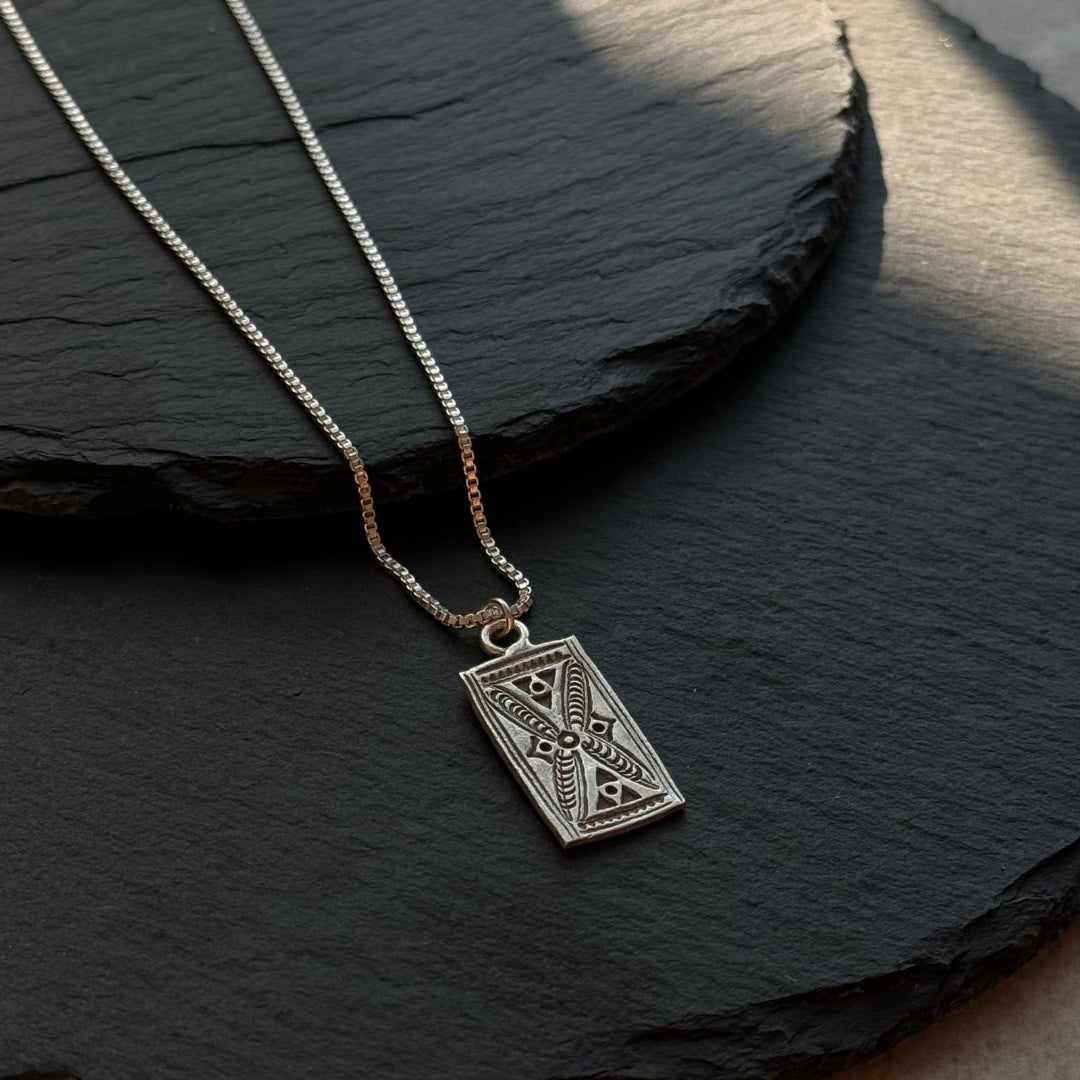 Silver necklace with a geometric pendant on a dark stone surface