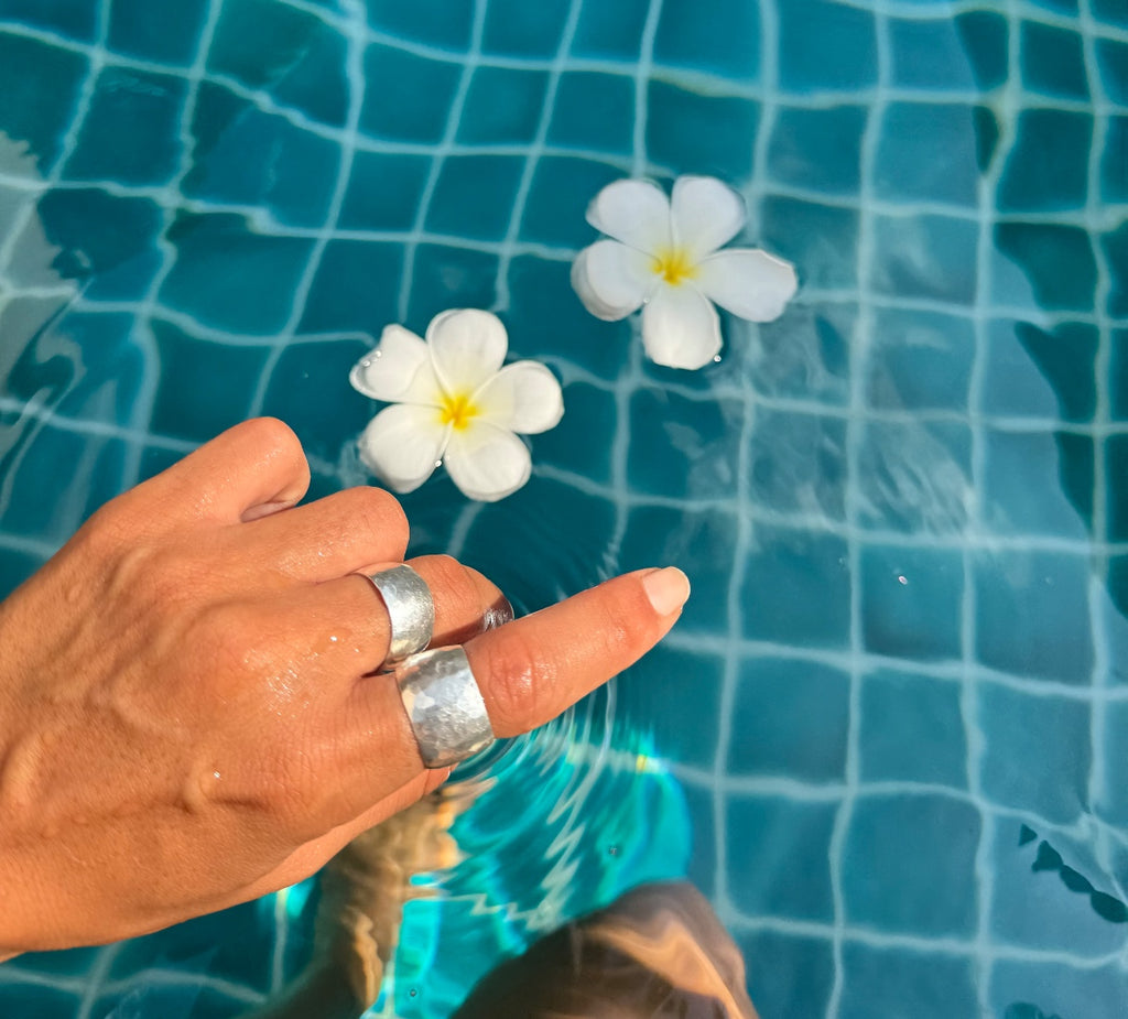 Hand with silver rings holding white flowers above a pool with blue tiles.
