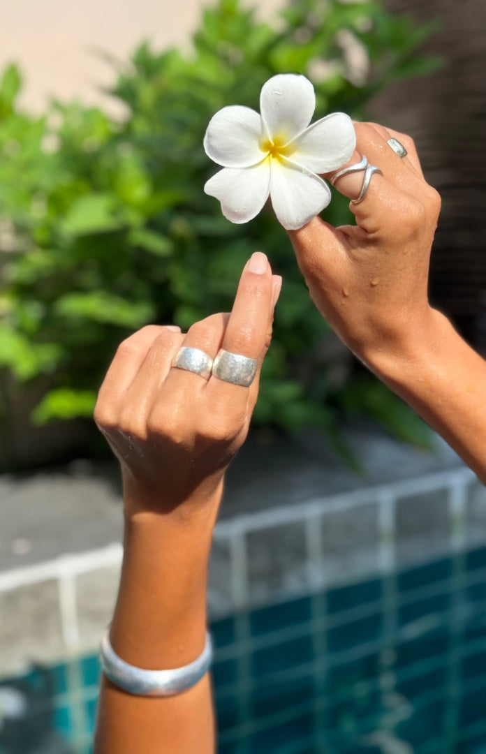 Two hands holding a white flower with a blurred pool and greenery in the background