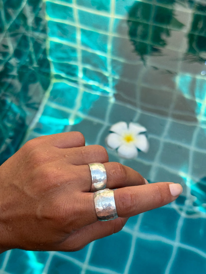 Hand wearing a silver ring with a pool and flower in the background