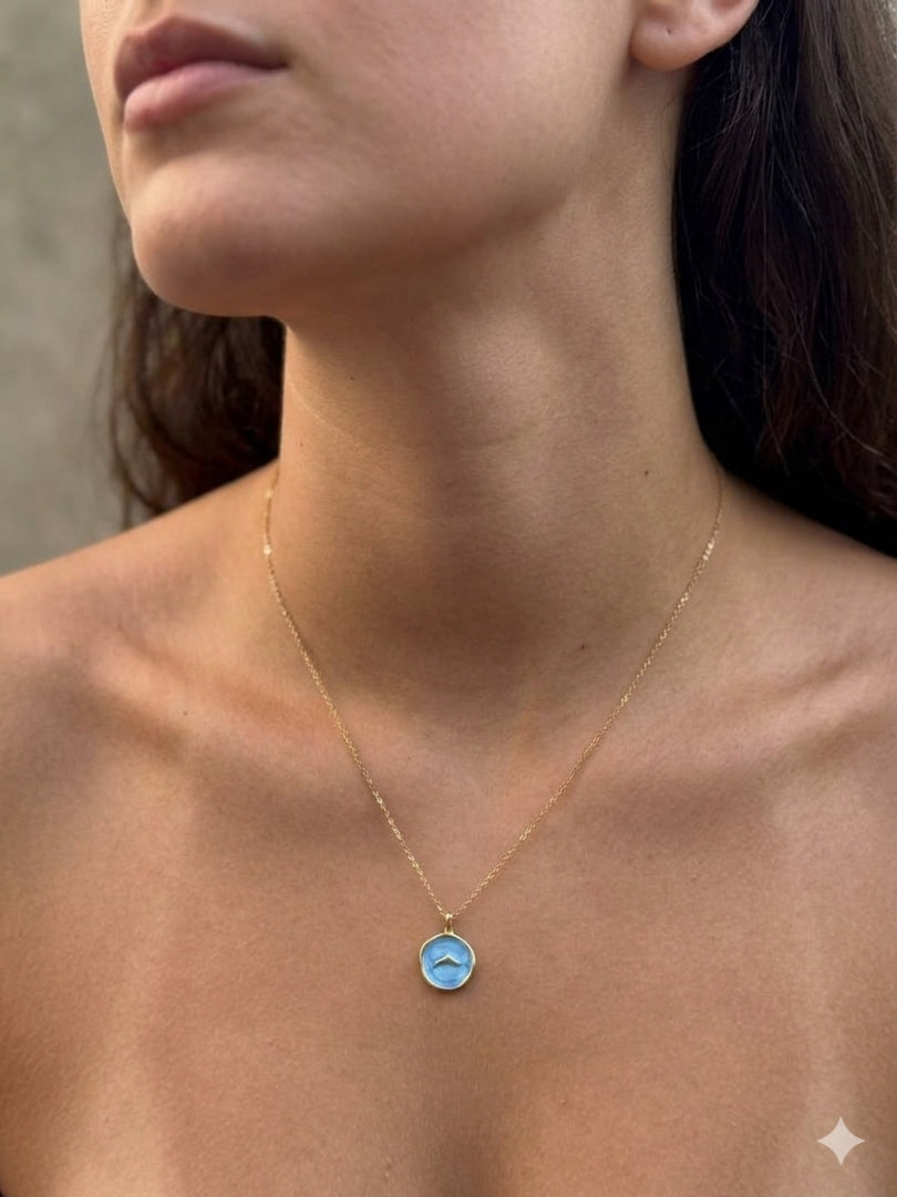 A close-up lifestyle shot of a model wearing a delicate gold chain necklace with a small circular pendant featuring a light blue background and a white stylized bird silhouette.