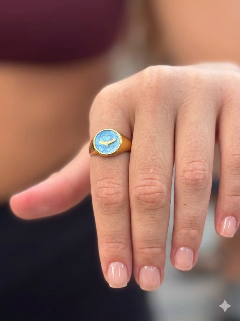 Close-up of a hand wearing a gold ring with a blue stone.