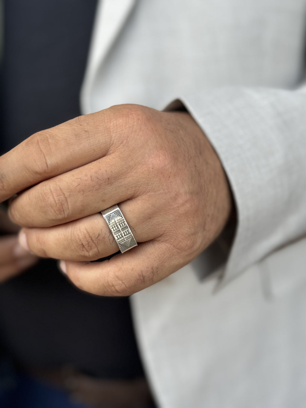 Hand wearing a silver ring with a detailed design, blurred background