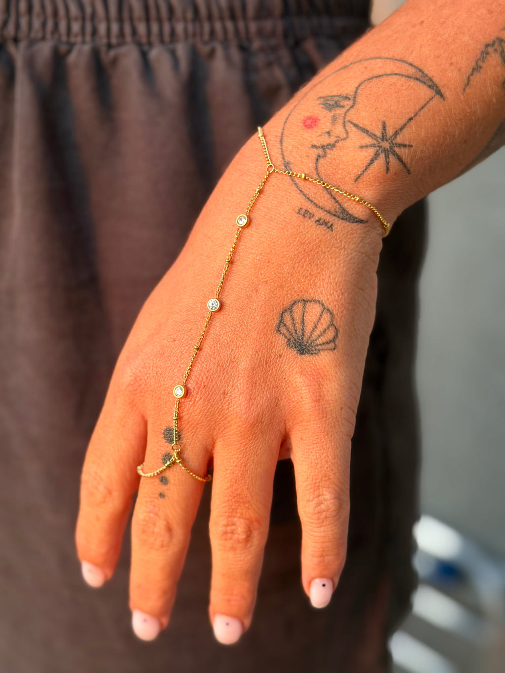 Hand with gold bracelet and tattoos wearing a brown garment