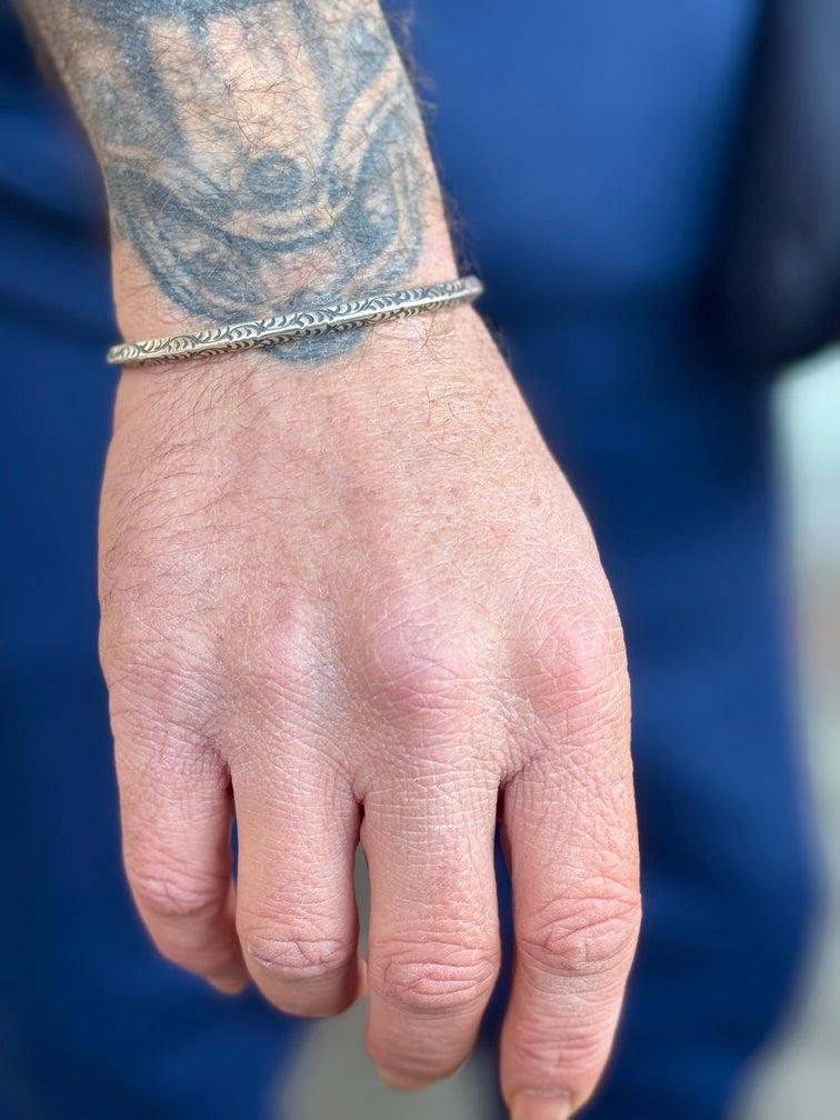 Hand with a silver bracelet and tattoo on a blue background