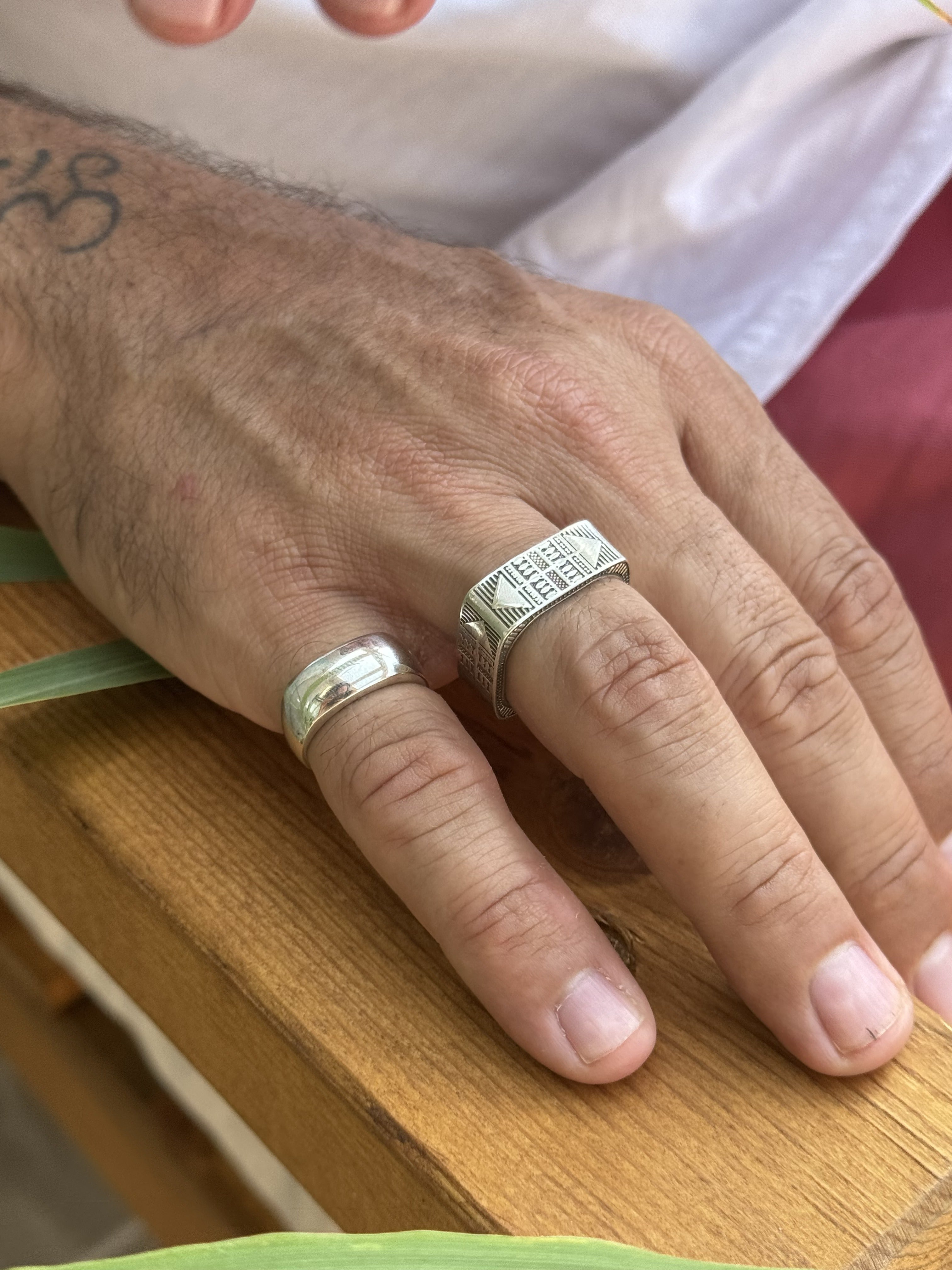 Hand wearing two silver rings on a wooden surface