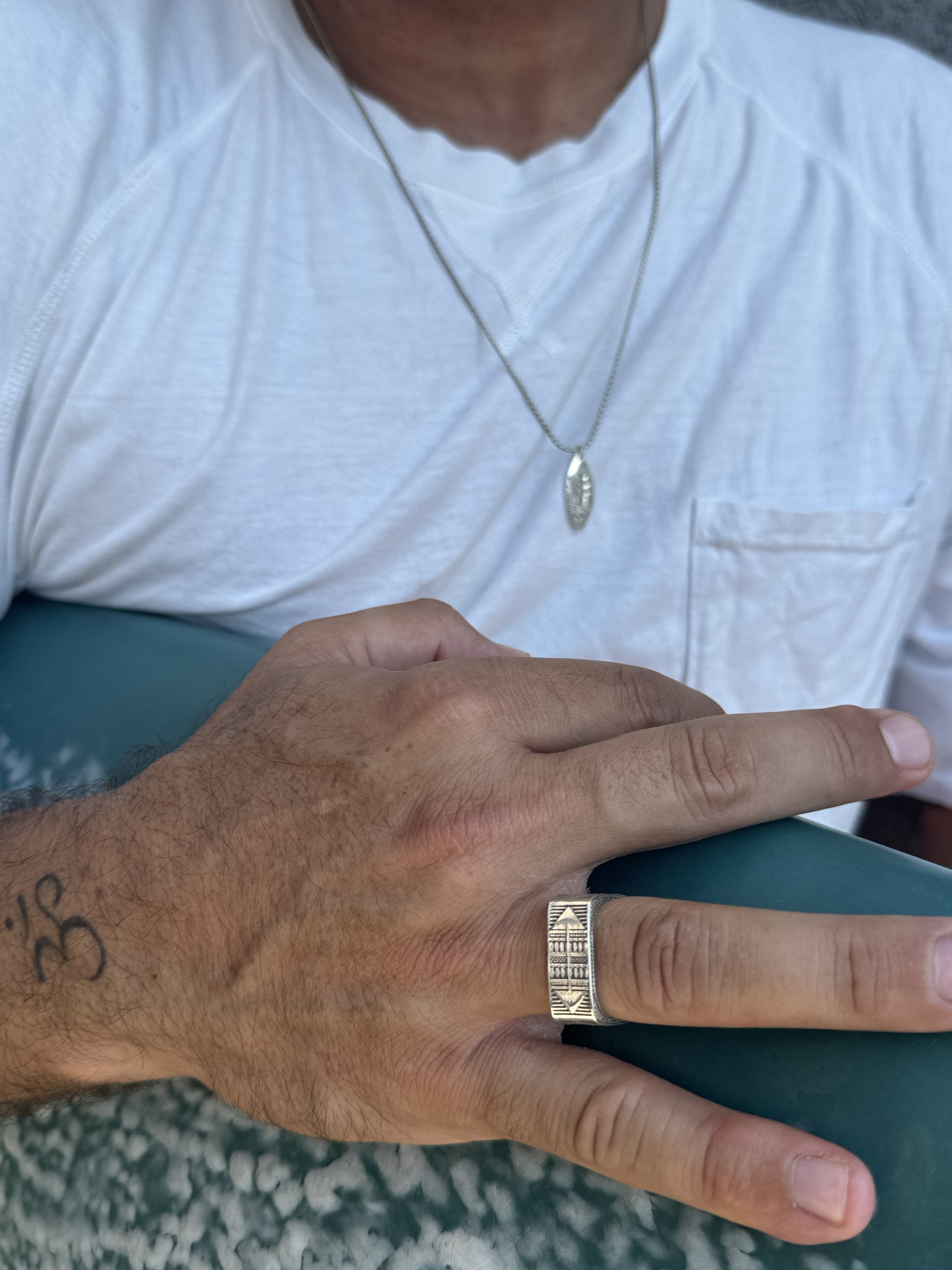 Hand with a gold ring and Om tattoo on a white shirt background