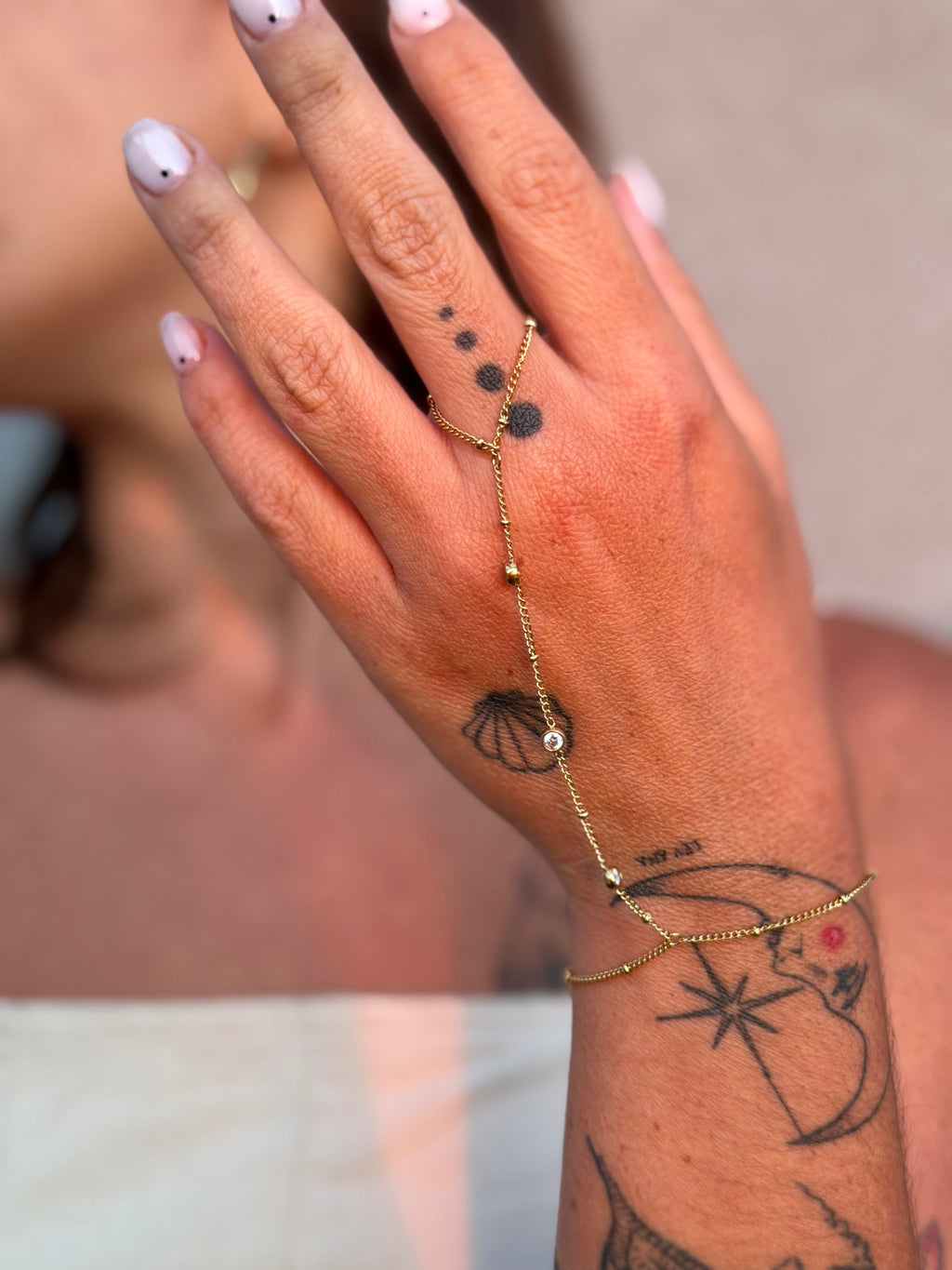 Hand with gold bracelet and tattoos against a blurred background