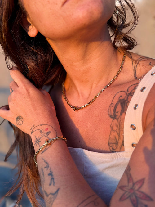Close-up of a person with tattoos on their arm and neck, wearing a gold necklace and bracelet.