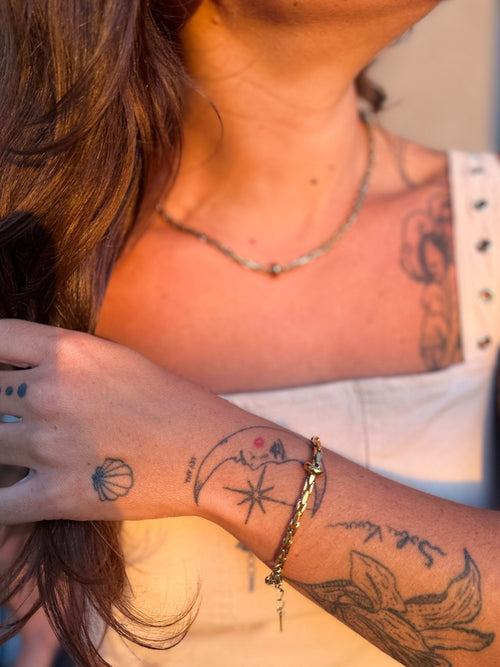 Close-up of a person with tattoos on their arm and neck, wearing a gold bracelet.