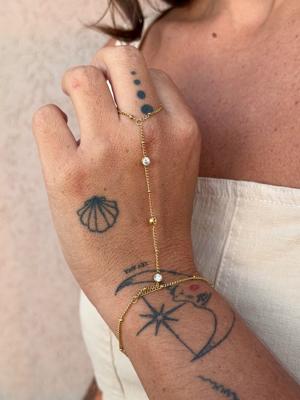 Hand with gold bracelet and tattoos on a neutral background