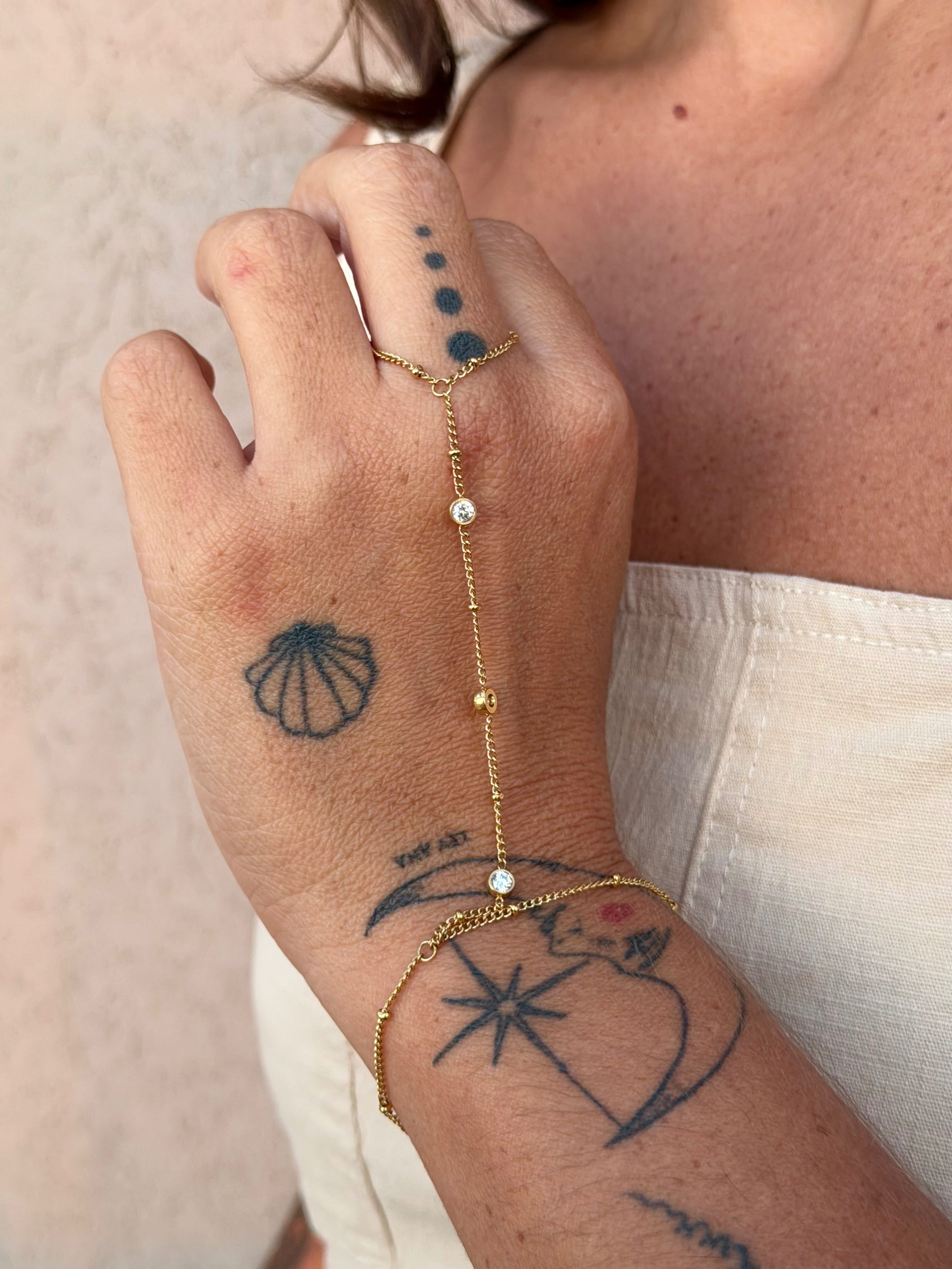 Hand with gold bracelet and tattoos on a neutral background